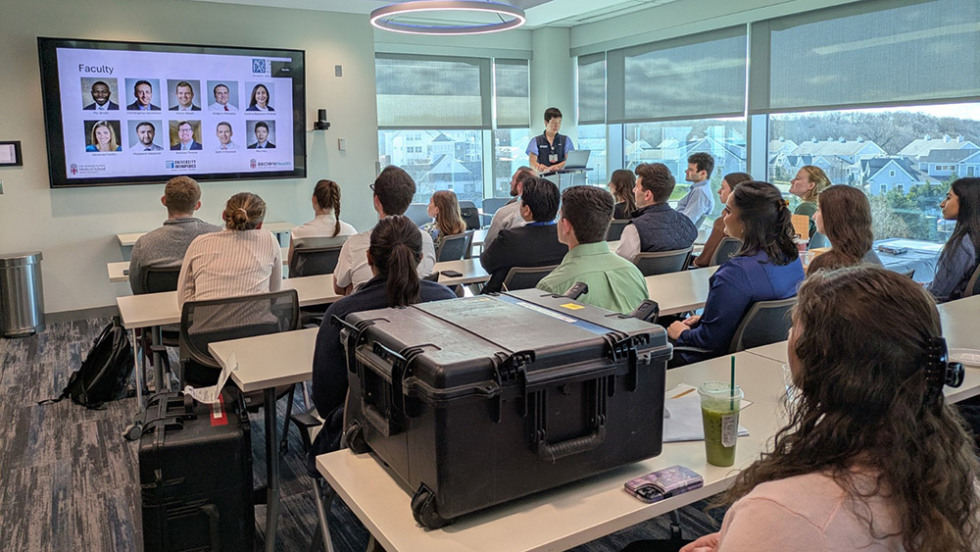 students in a classroom looking at a screen with an instructor speaking